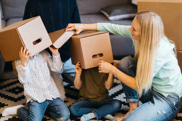 Picture of young married couple with indulging children sitting on floor among cardboard boxes