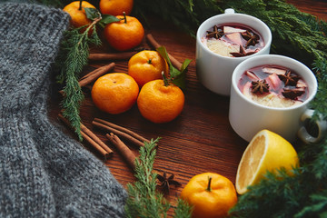 Christmas hot mulled wine in two small white cups with spices and citrus fruits on a wooden background and coniferous branches, top view