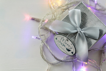 Top view of silver gift box and Christmas lights on white table