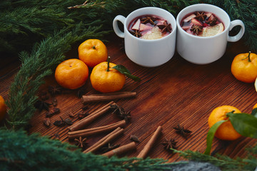 Christmas hot mulled wine in two small white cups with spices and citrus fruits on a wooden background and coniferous branches, top view