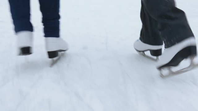 Two people legs running on ice-skating with white leather figure skates, close up rear action view