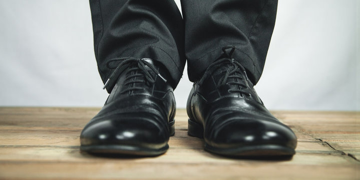 Man feet in black leather shoes stands on wooden floor.