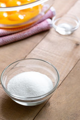 Dish of sugar with a bowl of baking ingredients and egg yolks in the background