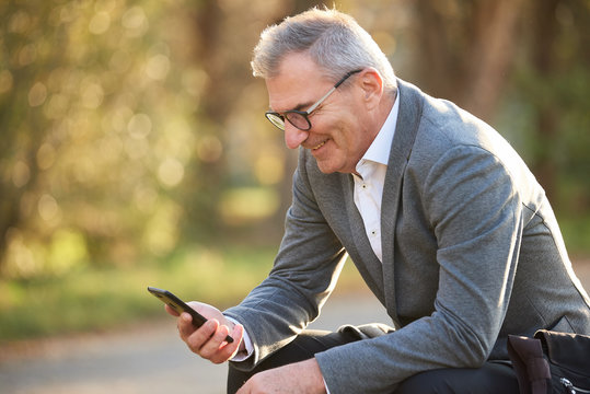 Business Mann schaut in sein Handy und sitzt im Gr&uuml;nen Park