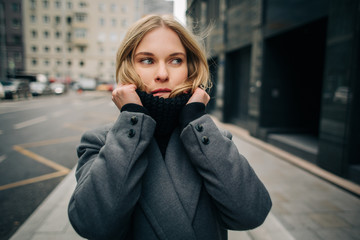 Fototapeta premium Photo of young blonde in gray coat on blurred background of city, road