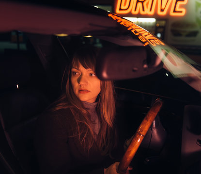 Young woman in car near refueling and building with Kibiniai drive inscription