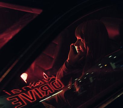 Young woman in car with smartphone and reflection of Kibiniai drive inscription