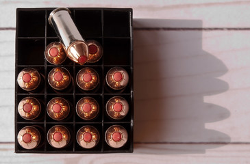 Fifteen 44 special bullets with red tips in a case with one of the bullets on top and several open spots in the case on a wooden background shot from above. 