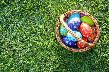 Flat lay shot of Easter eggs in the wicker basket on green spring grass. Space for text