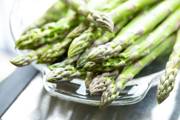 Macro close up on raw asparagus spears in a glass dish - obrazy, fototapety, plakaty