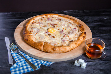 Pizza Carbonara with egg and ham on dark wood background