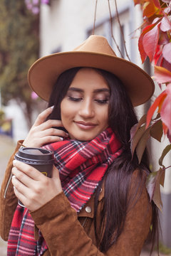 Young beautiful Turkish woman walks in a European city. A girl holds a glass of coffee. Happy brunette in a hat. Autumn. Fashion. Winter.