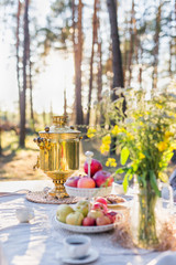 Traditional samovar on the table with apples and flowers outdoors