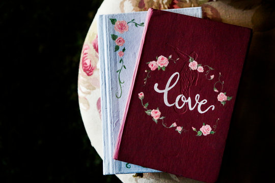 Libri color amaranto e bianco con scritto sopra Love e fiori decorativi su sfondo nero