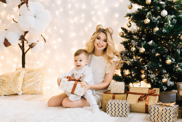 Happy family at home in front of the tree. Beautiful mother with a child open gifts. A woman and a little boy are preparing for the new year holidays