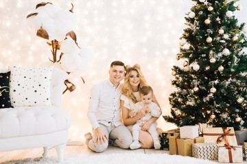 Portrait of a beautiful young family against the backdrop of the Christmas tree. Attractive parents and little son celebrate New year and smile