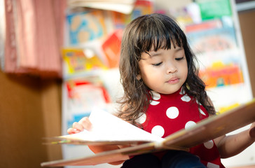 A cute little child Asian girl reading a book. Kid enjoy learning with happiness at home....