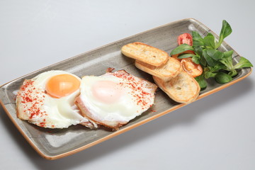 Two fried eggs with some bread and salad next to them