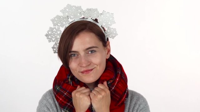 Happy Christmas woman in snowflakes headband wearing winter scarf. Beautiful cheerful woman enjoying winter holidays adjusting her scarf. Coziness, warmth concept