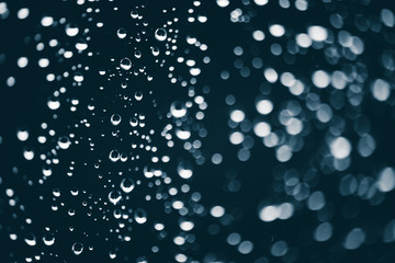 Dirty window glass with drops of rain. Atmospheric blue background with raindrops in bokeh. Droplets and stains close up. Detailed transparent texture in macro with copy space. Rainy weather.