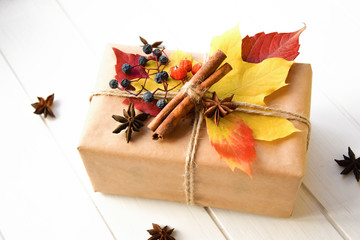 Handcraft gift box in the white wooden table. Autumn frame with gift, autumn leaves, cinnamon sticks, anise stars and nuts. Holiday gift on Thanksgiving