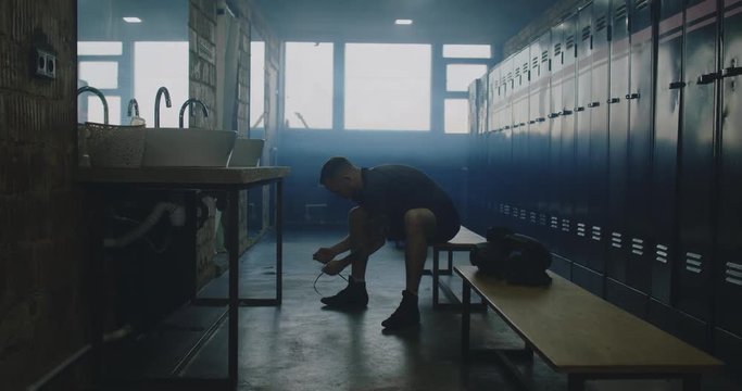 MS DOLLY IN Caucasian male ties his sport shoes in locker room before boxing martial arts training. 4K UHD 60 FPS SLOW MOTION