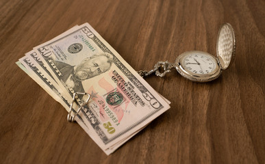 Clock and banknotes on brown table. Time is money concept