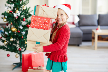 Cheerful child with stack of packed gifts preparing for Christmas eve at home