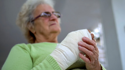 Old woman massage her injured broken hand sitting, cinematic dof