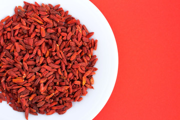 Goji berries in the white plate on red background.Top view.Copy space.