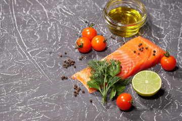 A piece of salmon on a gray background, tomatoes, dill, olive oil, lemon. Selective focus, space for text.