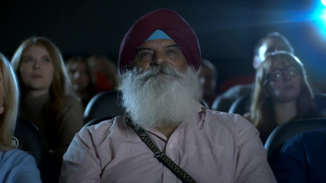Indian man at the movie theatre watching a film smiling and laughing