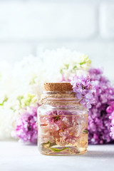 Obraz na płótnie Canvas Glass jar with aroma oil and with lilac flowers for spa and aromatherapy. Spa concept.