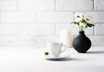A cup of hot coffee and a bouquet of camomiles in a vase.