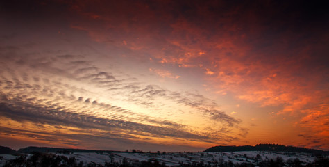 Colorful sunset in winter over hills forests in countryside village