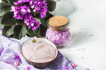 Obraz na płótnie Canvas spa setting with cosmetic cream, bath salt and African violet in flower pot on white wooden table background. Selective focus
