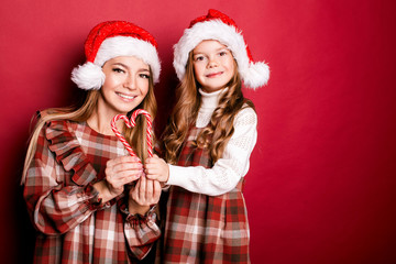 Happy smiling mother and daughter in  Christmas caps with  heart shaped sugar canes on the red background. Merry Christmas. Black Friday. Sale. Shopping 