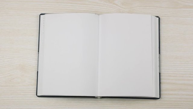 The hand of a businessman puts and opens an empty diary on the table.
