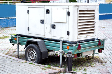 backup power generator mounted on a car trailer on wheels standing on a city street paved with paving slabs.