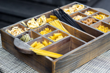 Wooden box with cells filled with traditional Italian food, pasta of different types in the assortment.