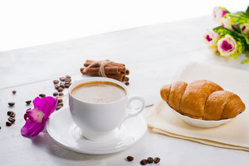 cup of coffee and a croissant on a served table with flower buds