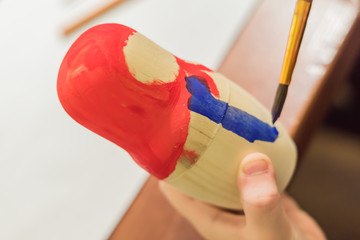 Kid decorating wooden doll toy (russian matrioshka) at the workshop