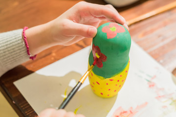 Kid decorating wooden doll toy (russian matrioshka) at the workshop
