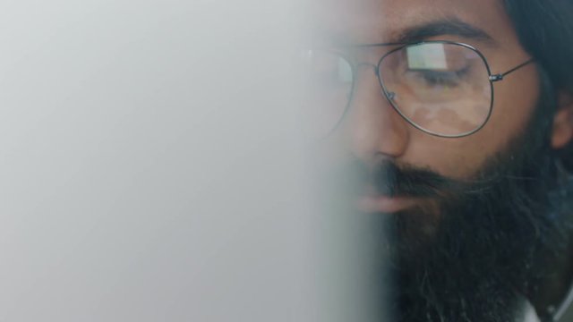 close up portrait young indian businessman using computer brainstorming browsing online research ideas for startup company project networking reading email wearing glasses in office