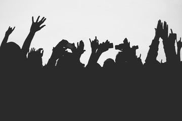 Fototapeta na wymiar Hands silhouettes of the crowd raised up at music show. Black and white picture