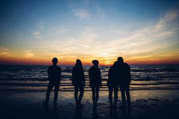 Group of friends watching sunset at the sea shore
