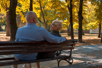 Senior man and woman sitting on a bench and having fun in park