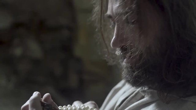 A man like Jesus Christ is digging a hole in the dungeon, a man is searching for a precious treasure, a man in a white robe is digging the earth with a stick and finds gold, Jesus hides the holy grail
