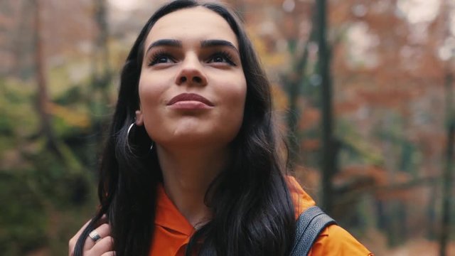 Close up brunette attractive young woman stand smile look around in forest outdoors with yellow leaves foliage autumn backpack hiker vacation portrait slow motion
