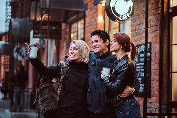 Cheerful friends standing together in an embrace near a cafe outside, looking away.